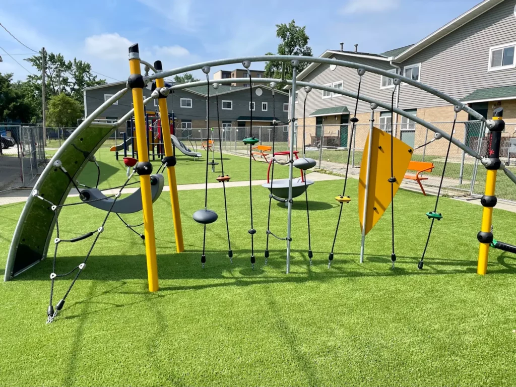 Modern playground with yellow climbing structure and rope elements on lush artificial turf at Washington Gardens municipal park.