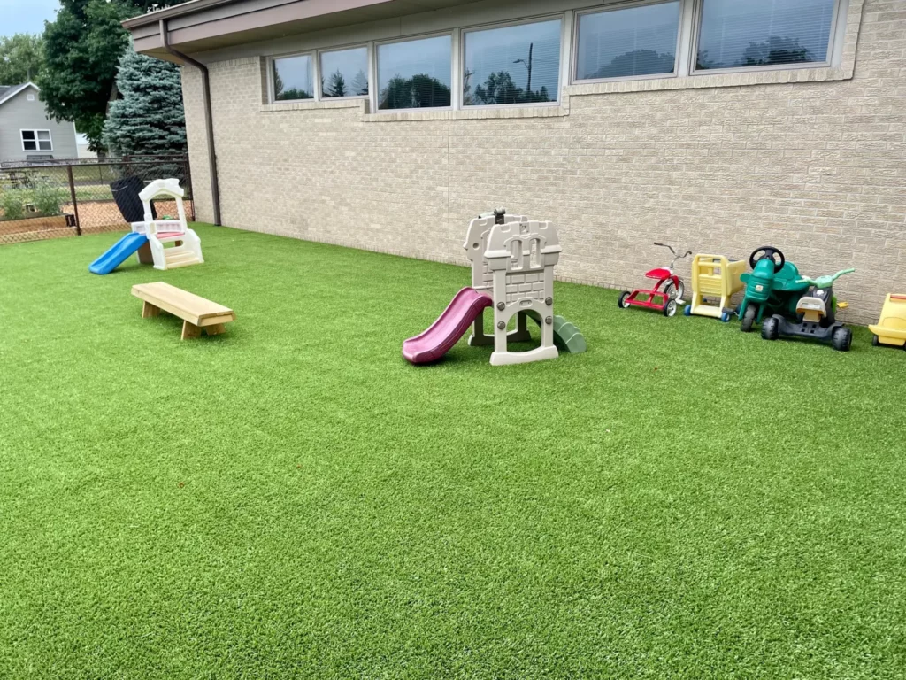 Artificial turf playground at Akron church with slides, ride-on toys, and bench on lush green synthetic grass surface.
