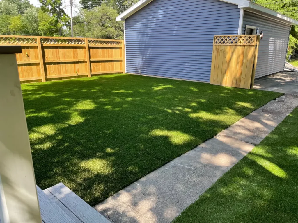 SportsGrass Edge XP artificial turf installed in fenced backyard beside blue garage with cedar gate and lattice topper.