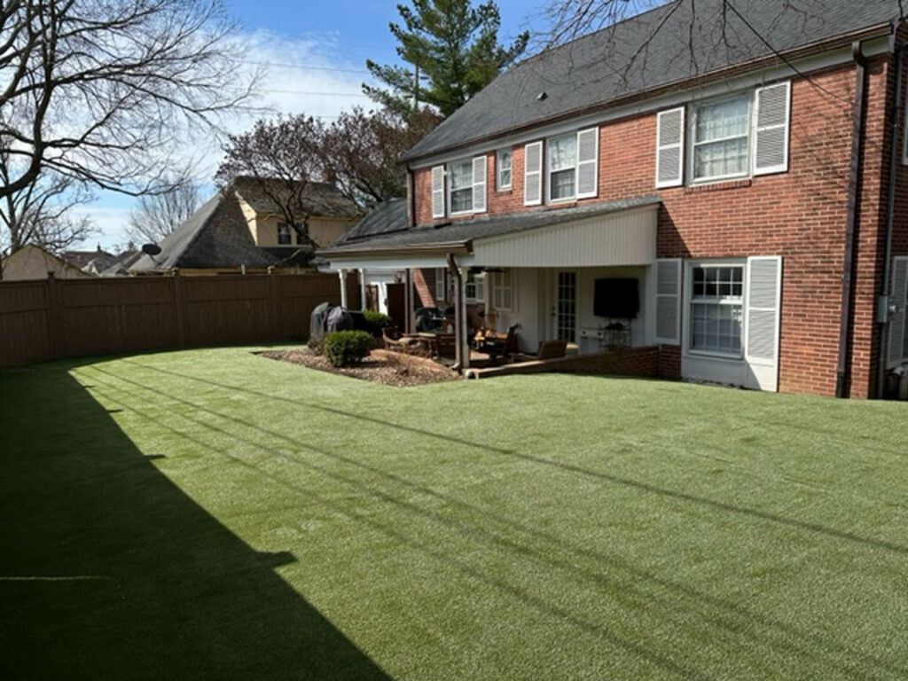 K9Grass Elite artificial turf installed in fenced suburban backyard beside brick home with covered patio, Columbus