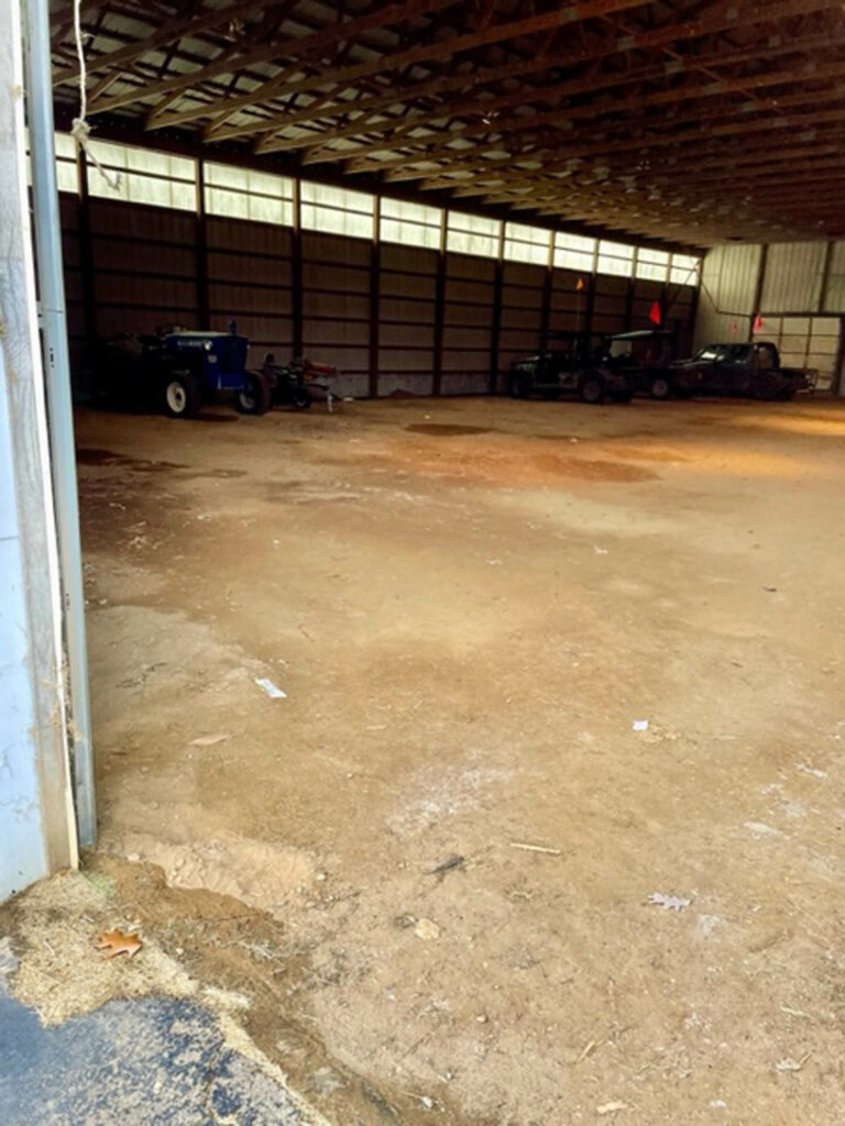 Large empty 6,000 sq ft metal pole barn with dirt floor awaiting SportsGrass turf installation in Three Rivers sports complex.