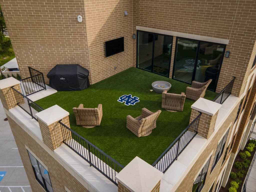 Rooftop terrace with 690 sq ft artificial SportsGrass turf, Notre Dame logo inlay, wicker chairs, fire pit, covered grill, and outdoor TV.