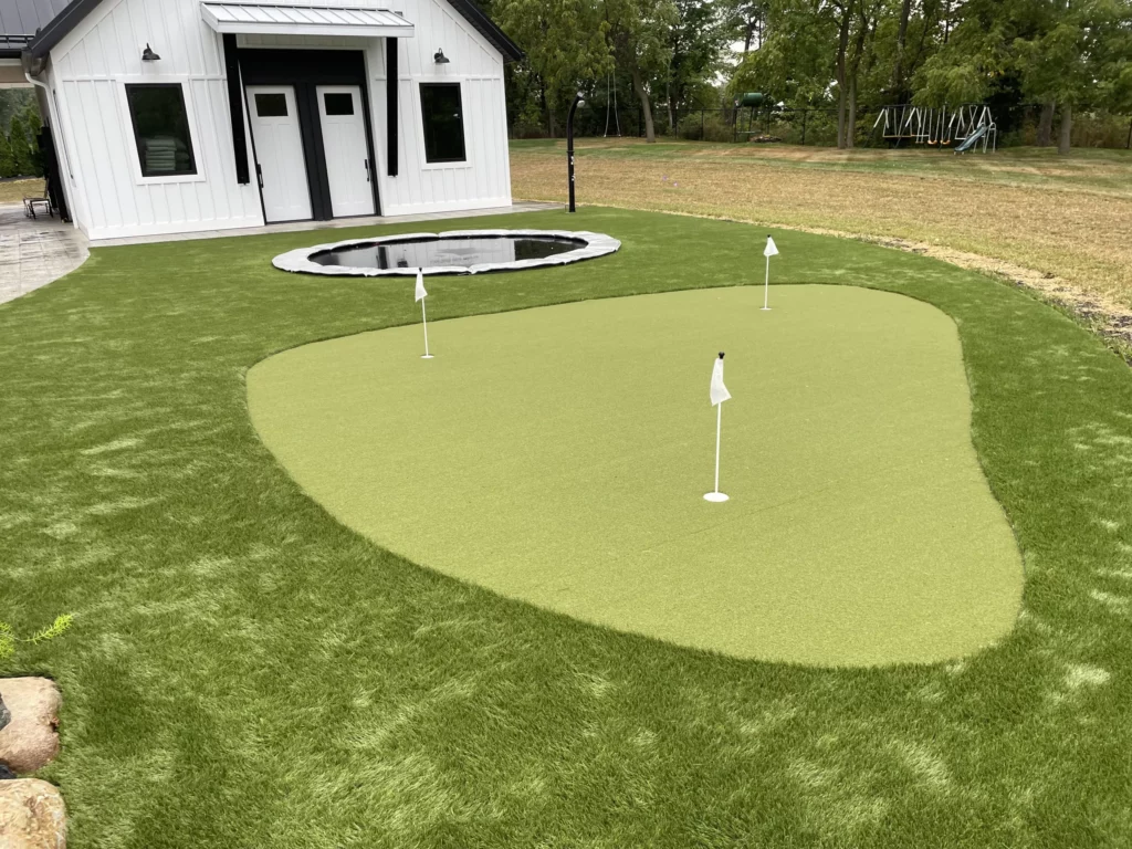 Backyard artificial putting green with 3 flags and inground trampoline beside modern white barn, Goshen IN