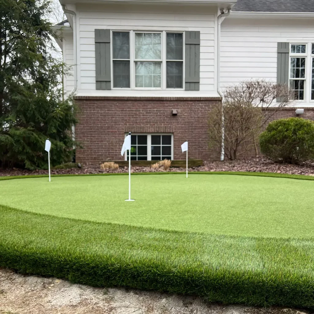 Backyard GolfGreens artificial putting green with 3 holes and white flags beside a brick and white siding home in Warsaw, IN.