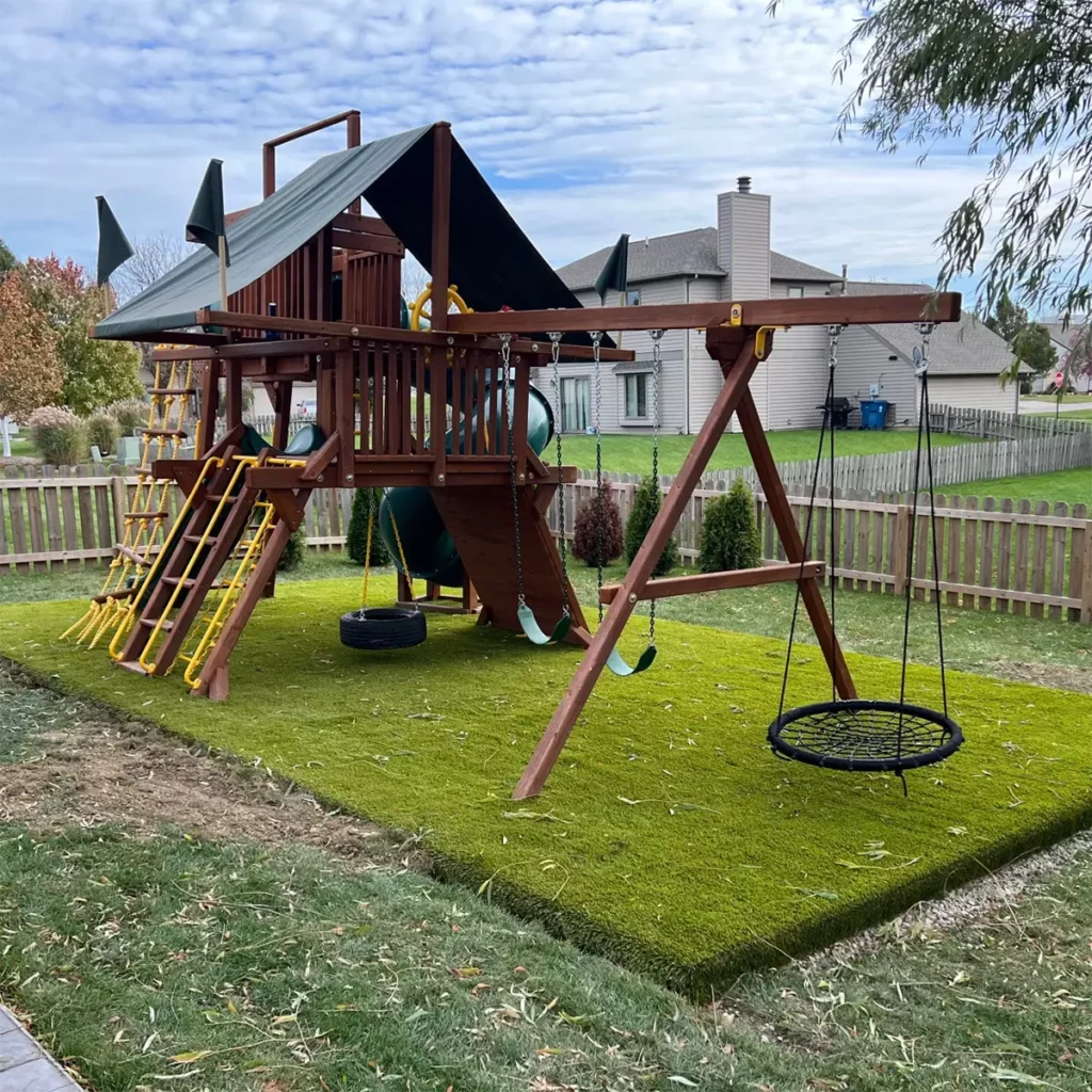 Residential backyard swing set on lush artificial Playground Grass Ultra turf in Fort Wayne, fenced yard with slide and swings.