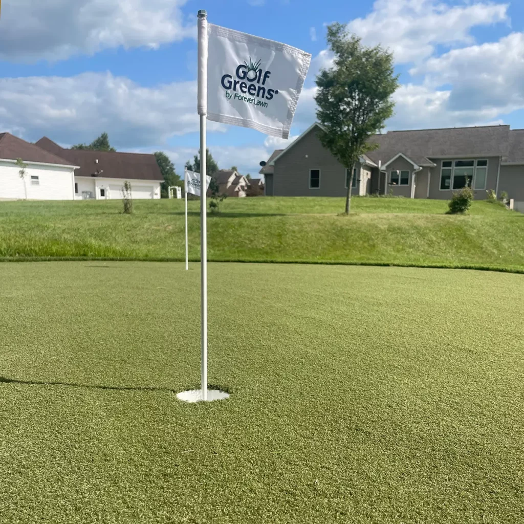 GolfGreens by ForeverLawn artificial putting green with flagstick in residential backyard, suburban homes in background.