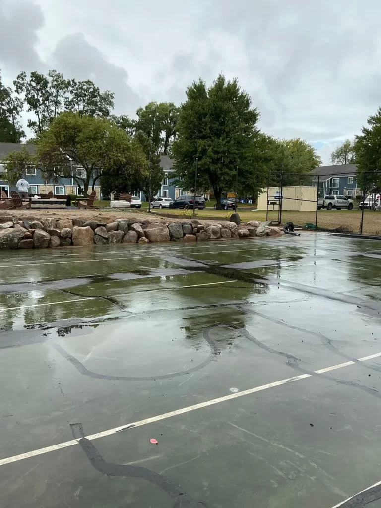 Wet sport court surface with rock border edging during K9Grass dog park installation, residential setting, South Bend, Indiana.