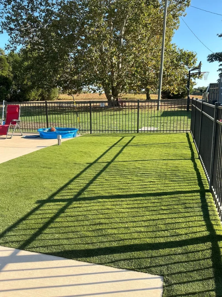 K9Grass Classic+ artificial turf pet yard with black metal fence, kiddie pool, and basketball hoop in Fort Wayne residential backyard.