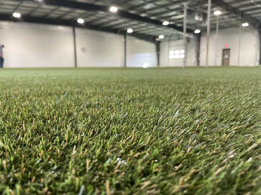 Indoor pet facility with K9Grass artificial turf installation covering large warehouse space with bright overhead lighting.