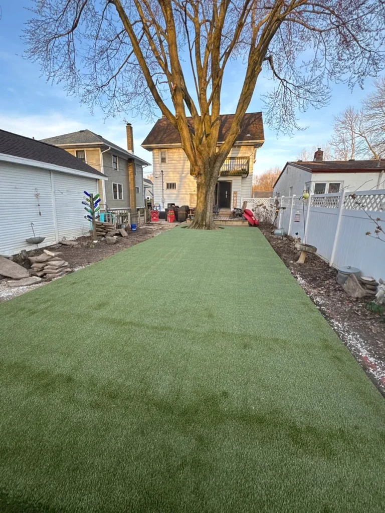 K9Grass artificial turf installed in narrow residential backyard beside white vinyl fence and large tree, Fort Wayne pet yard
