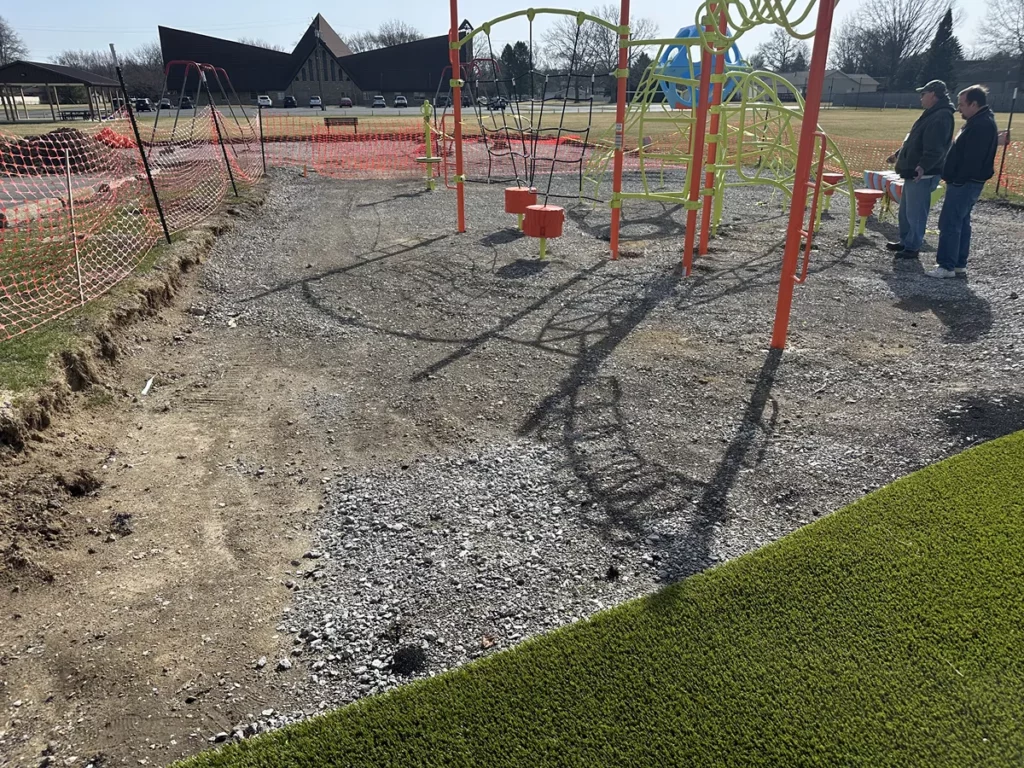 Playground Grass Ultra turf installation in progress at Hobart municipal park, with gravel base, orange safety fencing, and colorful play equipment.