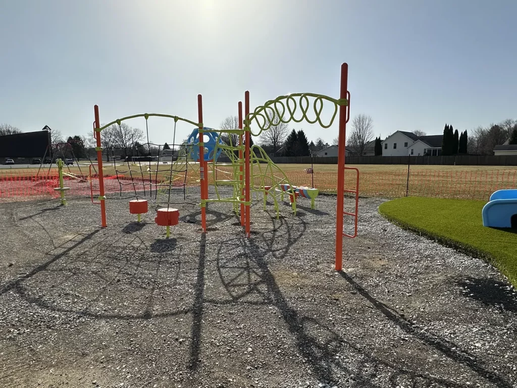 New municipal playground with orange and green climbing structures on gravel, bordered by synthetic turf, Hobart park setting.