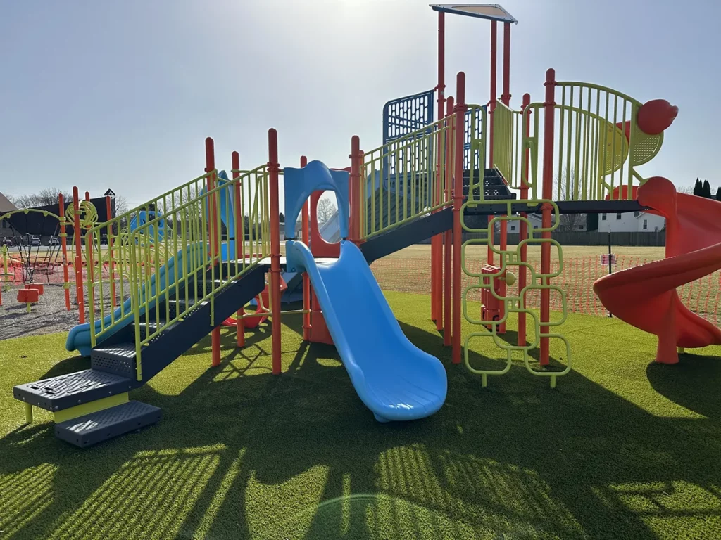 Colorful municipal playground with blue slide and red tube slide installed on lush artificial turf in Hobart park.