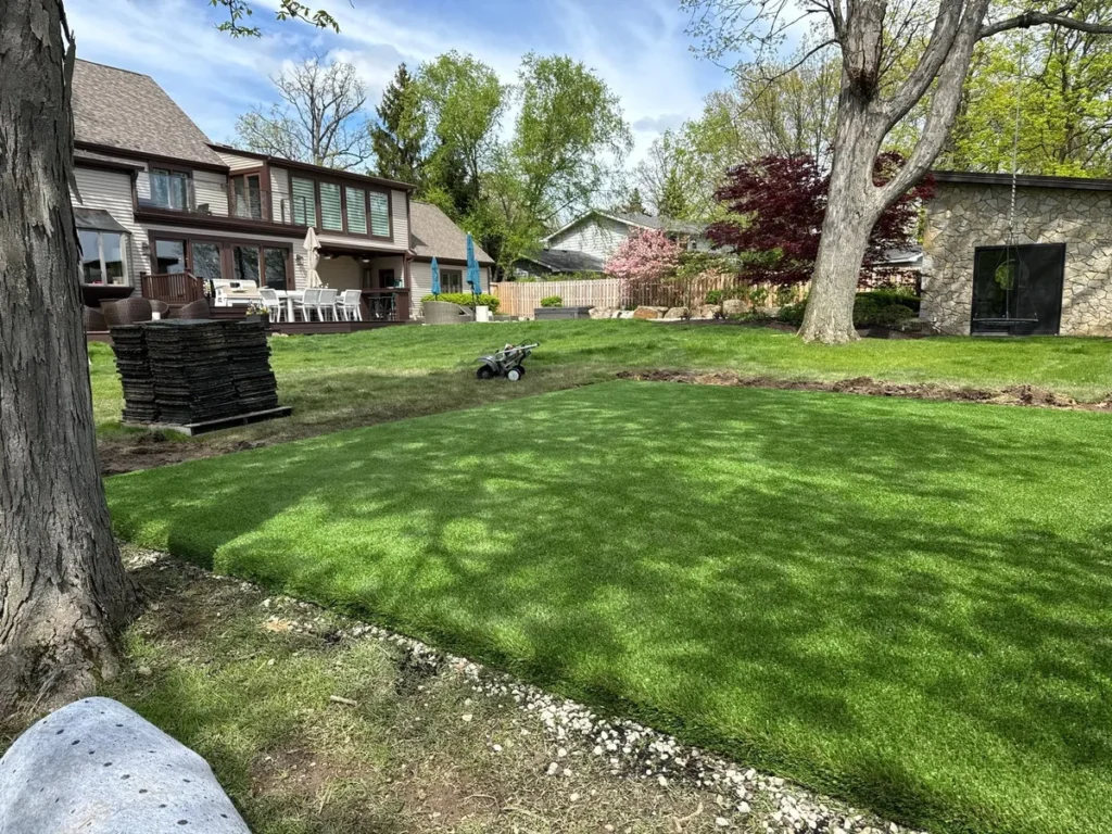 Lush green Playground Grass Ultra sod freshly installed in large suburban backyard with stacked turf rolls and compactor nearby.