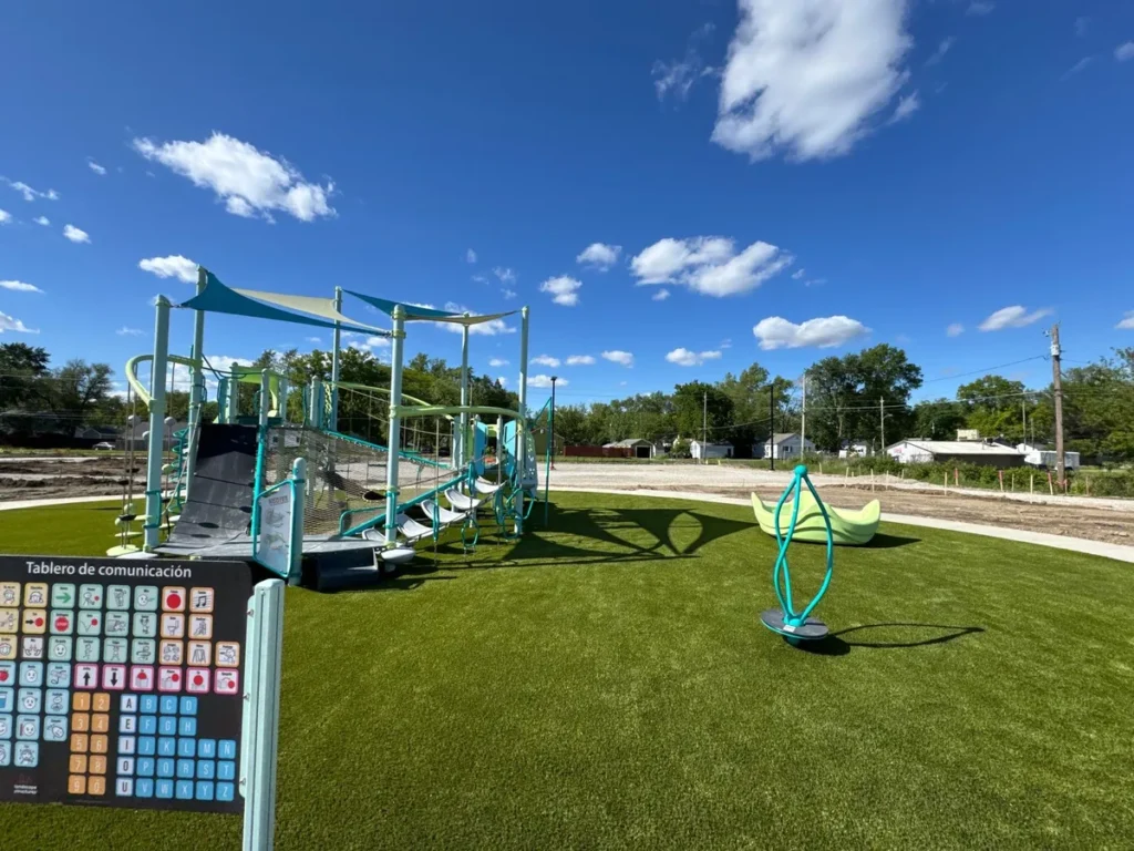 Modern teal playground with shade sails on Playground Grass Ultra artificial turf at Fort Wayne school, sunny day.