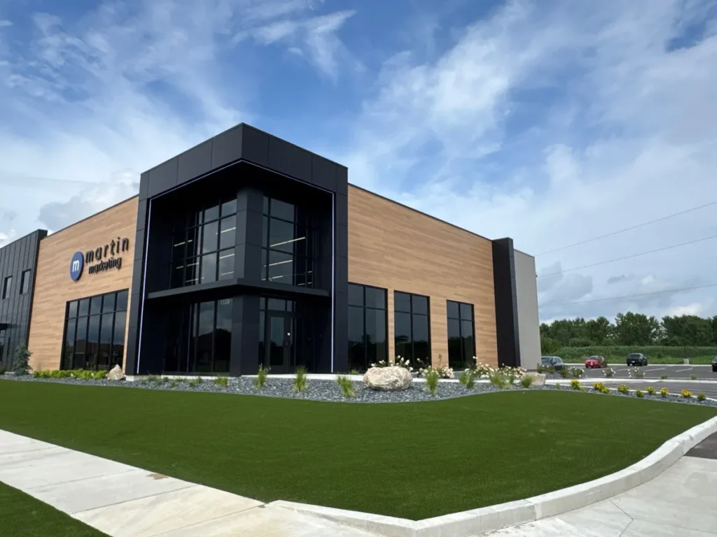 Lush artificial turf lawn with rock landscaping borders fronting a modern two-story commercial office building.