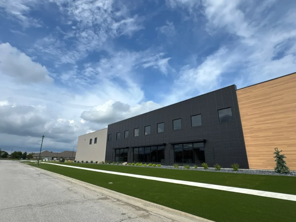 Modern commercial building exterior with lush artificial turf lawn, dark metal panel facade, wood accent siding, and decorative landscaping.