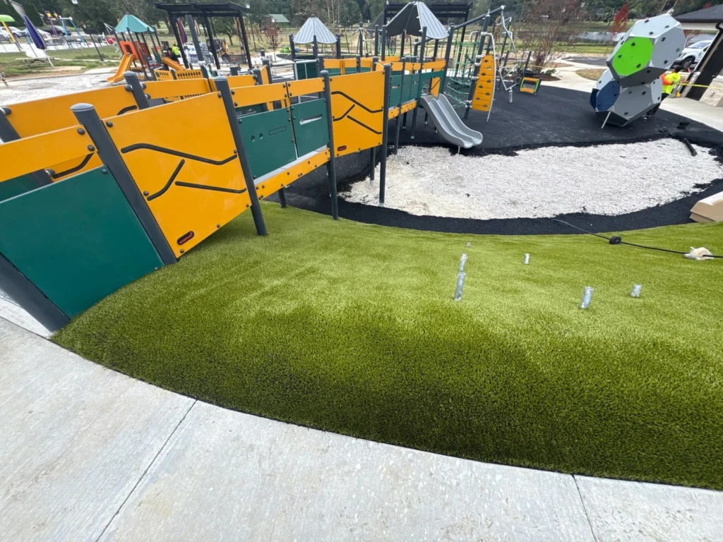 Artificial turf surrounds colorful yellow and green playground equipment at City Lake Park, Booneville municipal playground installation.