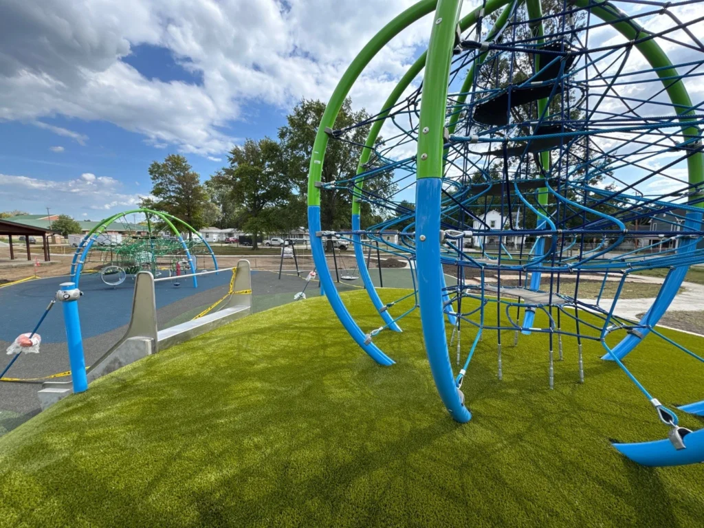Playground Grass Ultra artificial turf installed on rolling hills beneath colorful rope climbing structures at Herz-Rose Park.