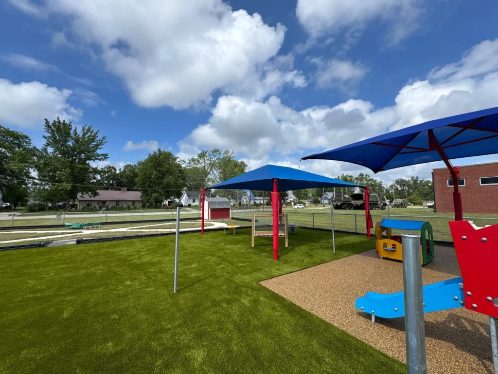 Artificial turf playground at Portland Head Start school with blue shade structures, colorful play equipment, and rubber safety surfacing.