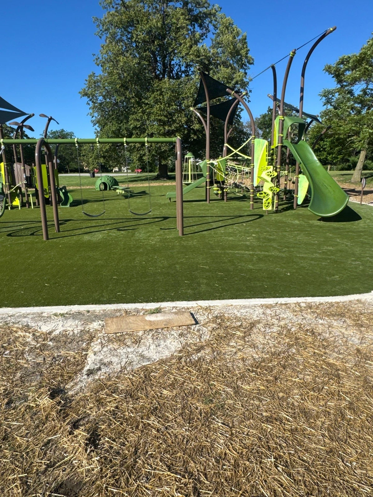 ForeverLawn Playground Grass Ultra installed at Hanna Homestead Park playground with green equipment, swings, slide, and shade sails.