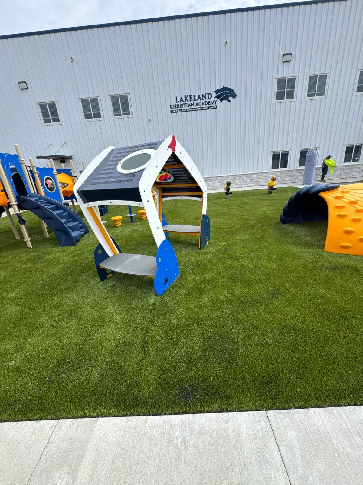 Artificial playground grass installation at Lakeland Christian Academy in Warsaw, IN with colorful play structures on lush green turf.