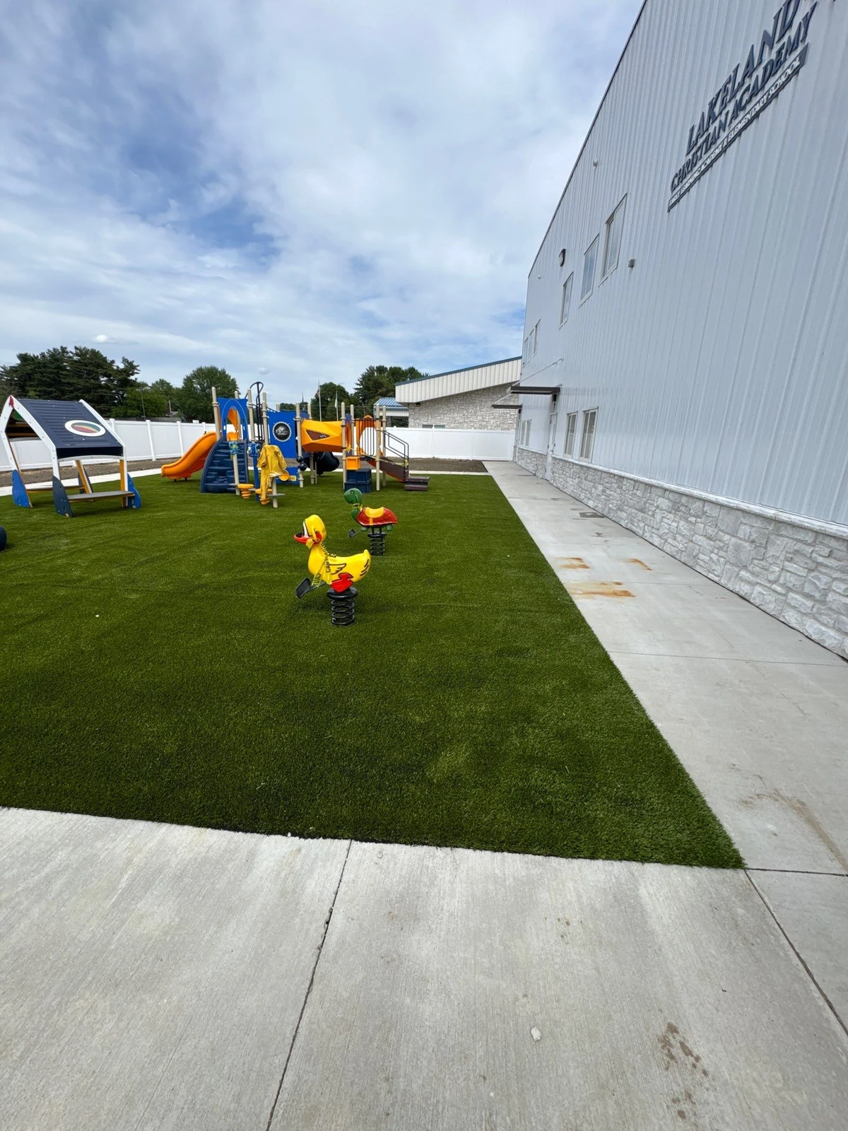 Artificial playground turf installation at Lakeland Christian Academy in Warsaw, IN with colorful play structures and spring riders.