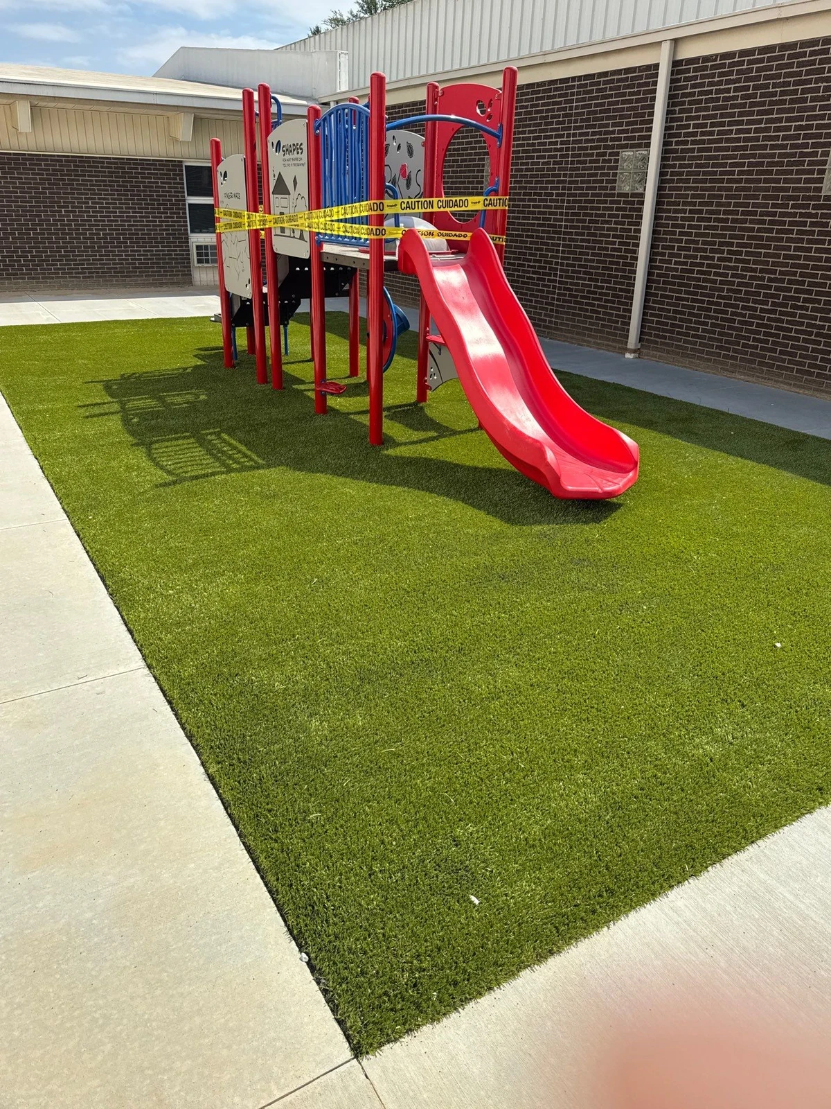 Red and blue playground with slide on ForeverLawn Playground Grass Ultra artificial turf at Lutheran Central School, Brownstown IN.