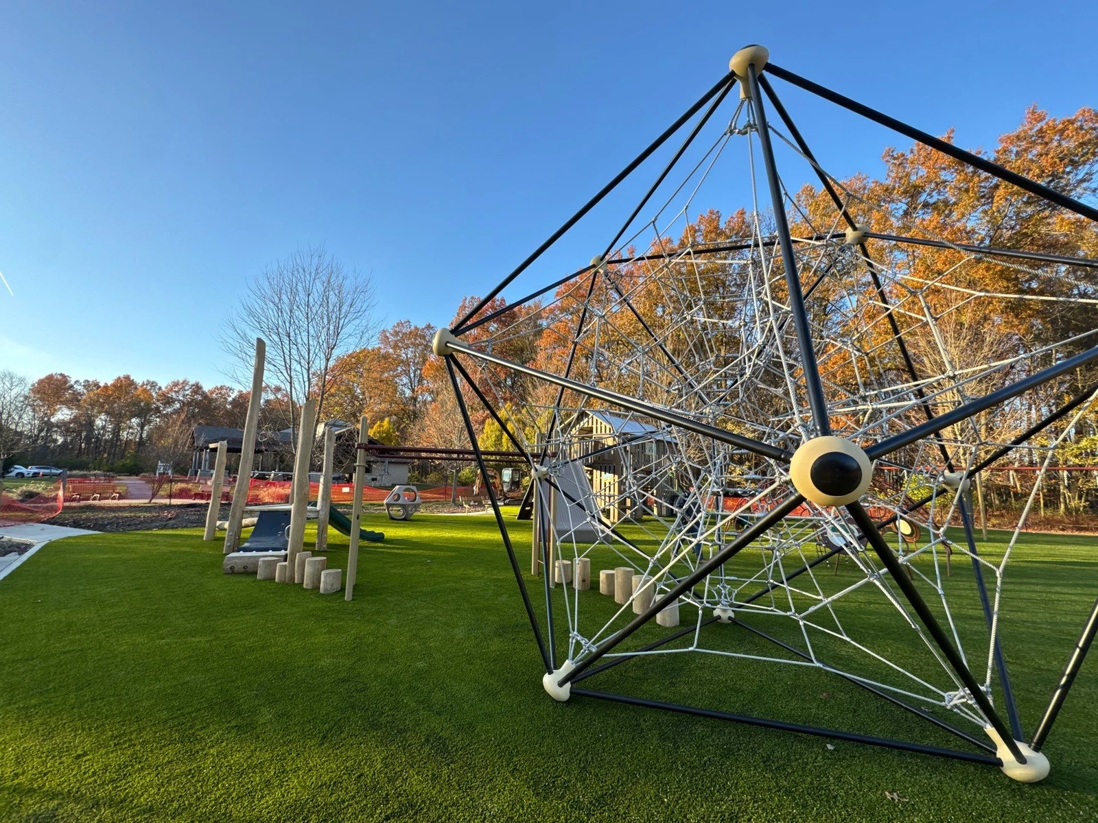 Modern rope climbing structure on lush artificial turf at McNamara Park playground, surrounded by autumn trees in Galena, OH.