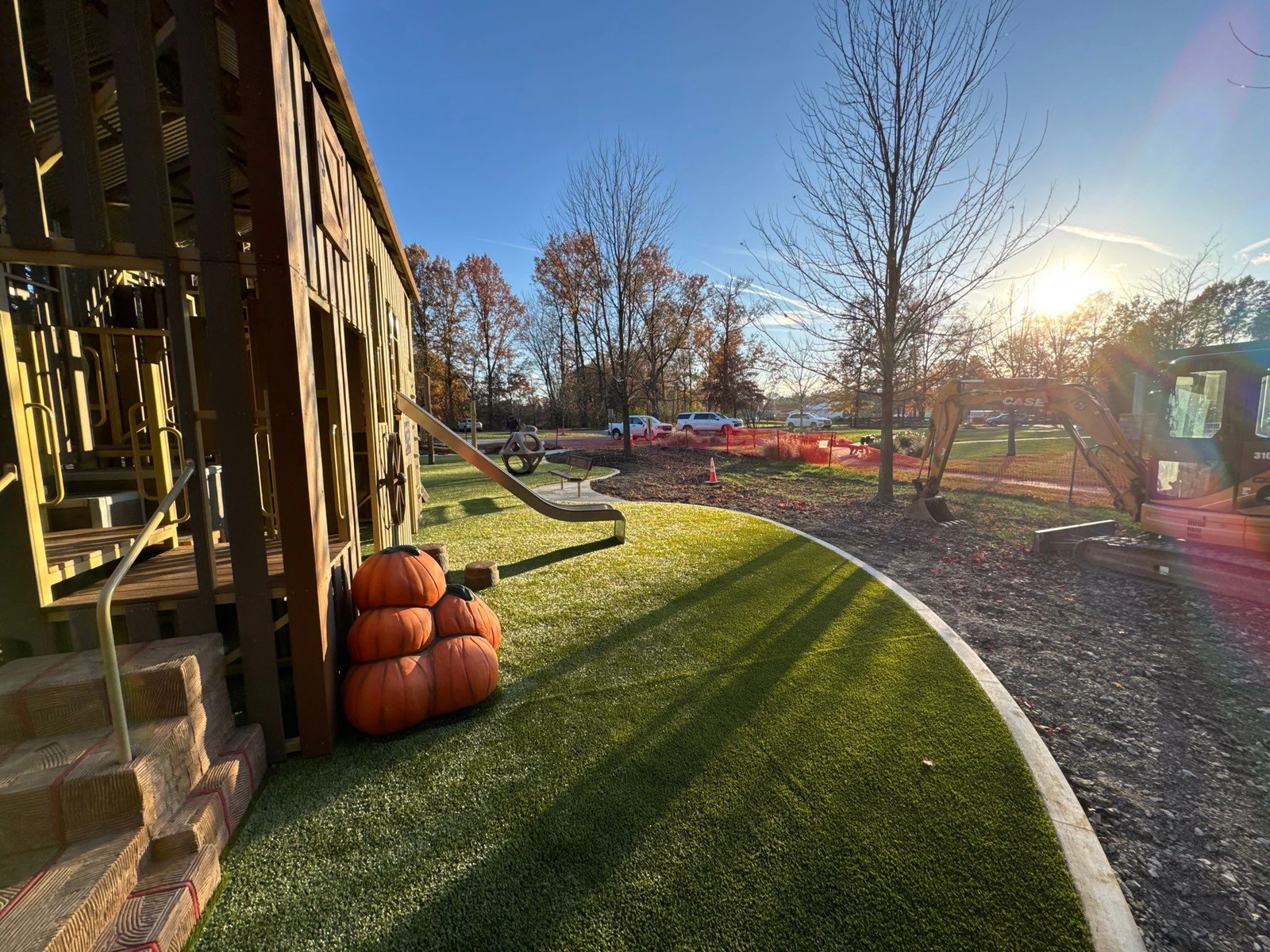 Artificial turf playground area with wooden barn structure, pumpkin decor, slide, and excavator nearby during fall installation, Galena OH.