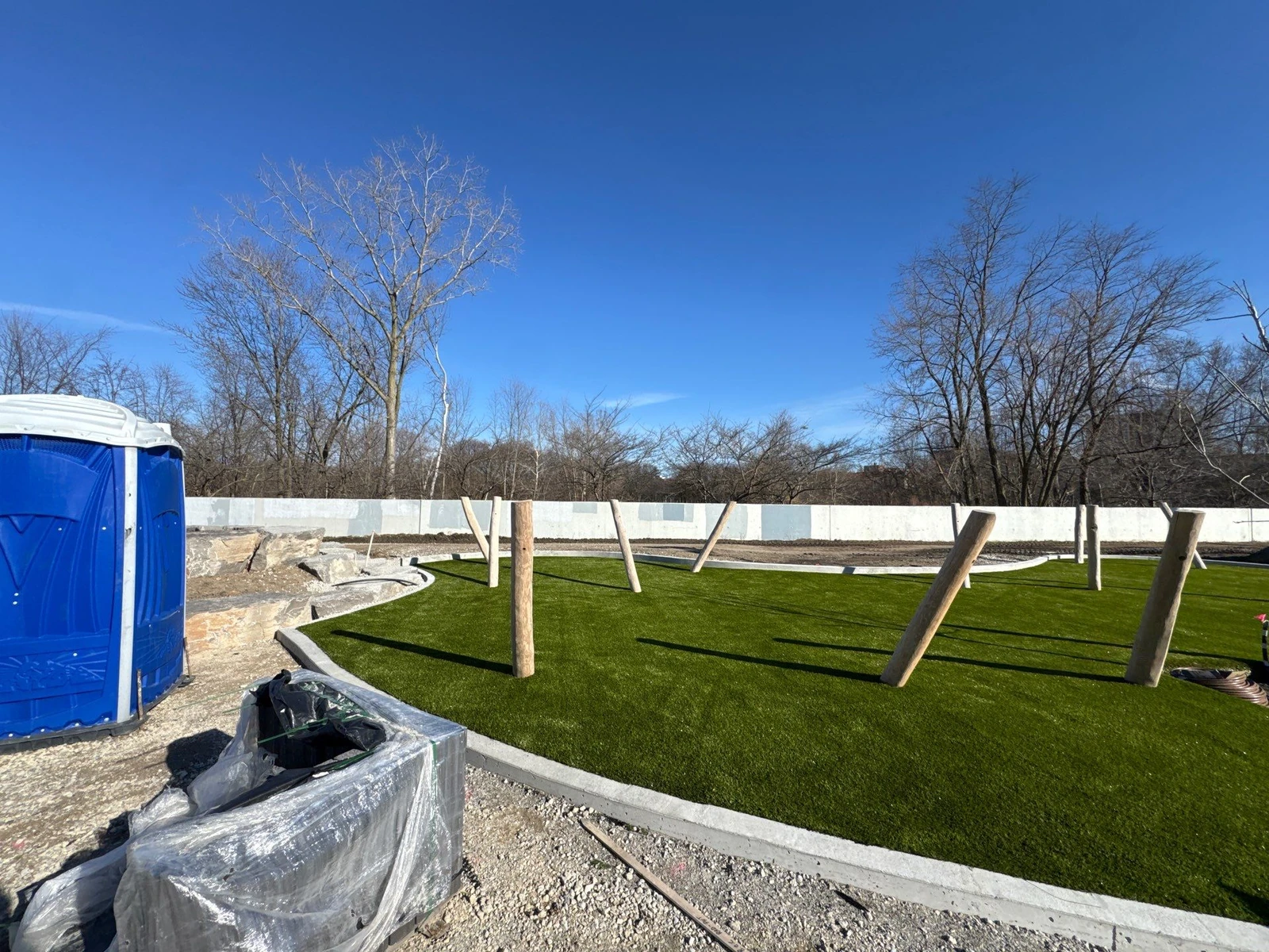 ForeverLawn Playground Grass Ultra installation in progress at Fort Wayne Riverfront park with timber play posts and white perimeter wall.