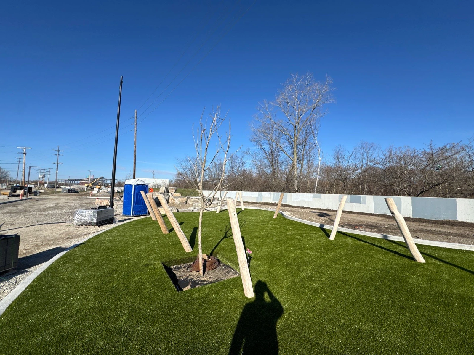 Newly installed artificial turf with staked young trees at Fort Wayne Riverfront Phase 2B municipal park construction site.