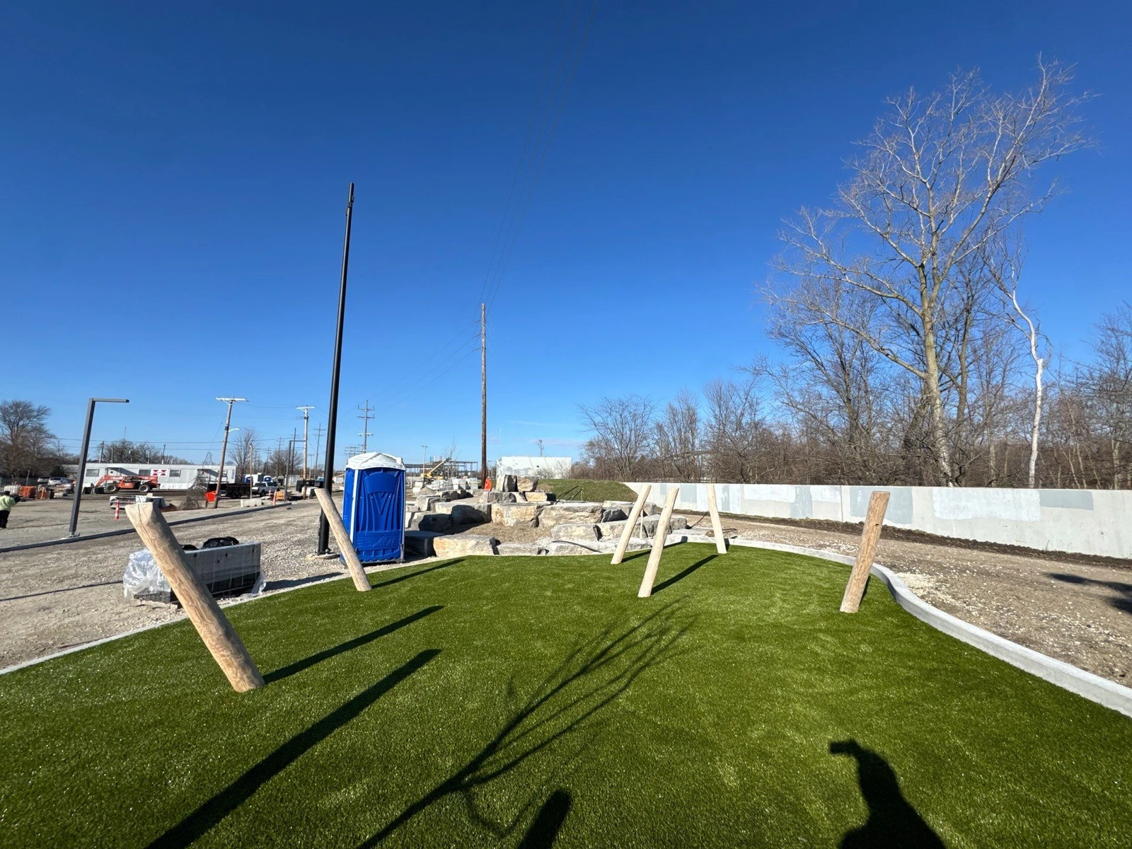 ForeverLawn Playground Grass Ultra installation in progress at Fort Wayne Riverfront Phase 2B, with timber posts and stone border.