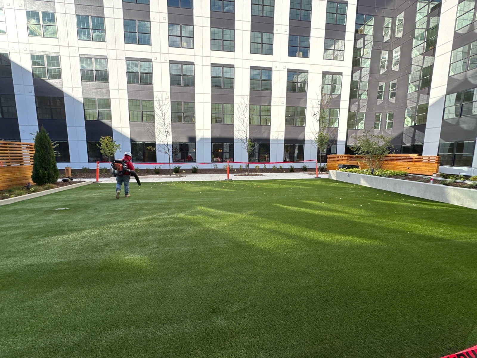 Lush artificial turf courtyard at Electric Works commercial complex with worker using leaf blower and modern building backdrop.
