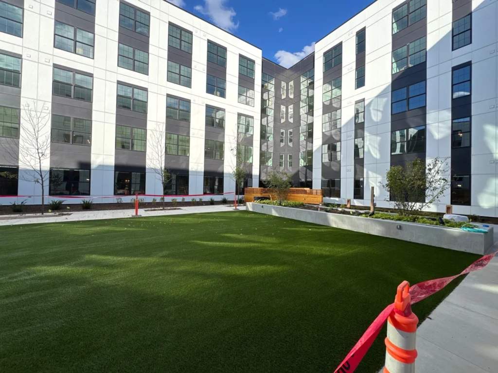 Lush artificial turf courtyard installed within a modern multi-story commercial building at Electric Works, with raised planters and young trees.