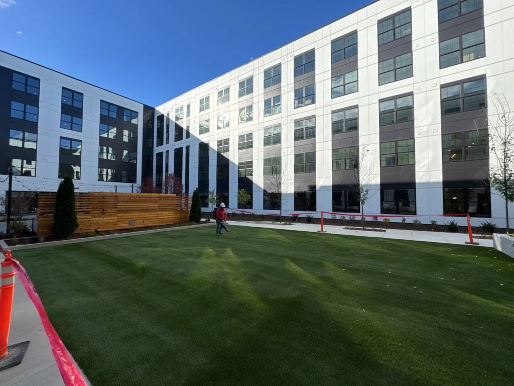 Lush artificial turf courtyard installed at Electric Works, surrounded by modern multi-story building with white and dark panels.