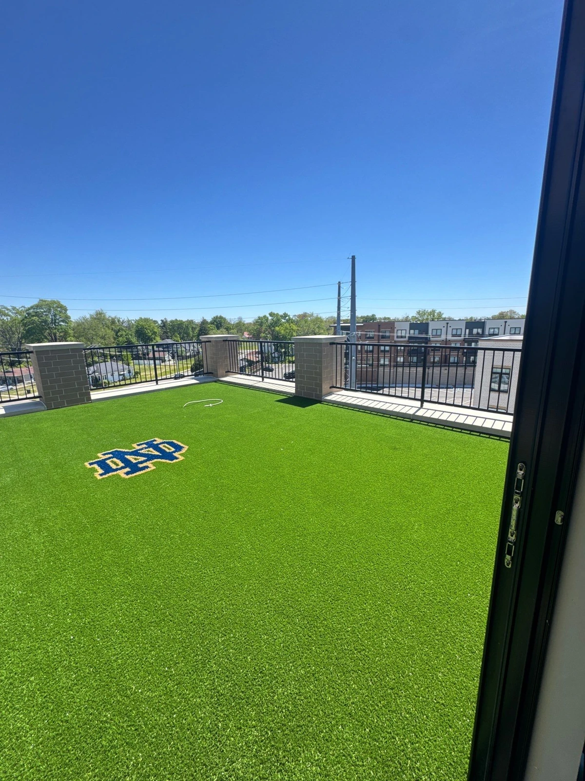 Rooftop artificial turf installation with Notre Dame ND logo inlay on 690 sq ft urban balcony with black metal railing.