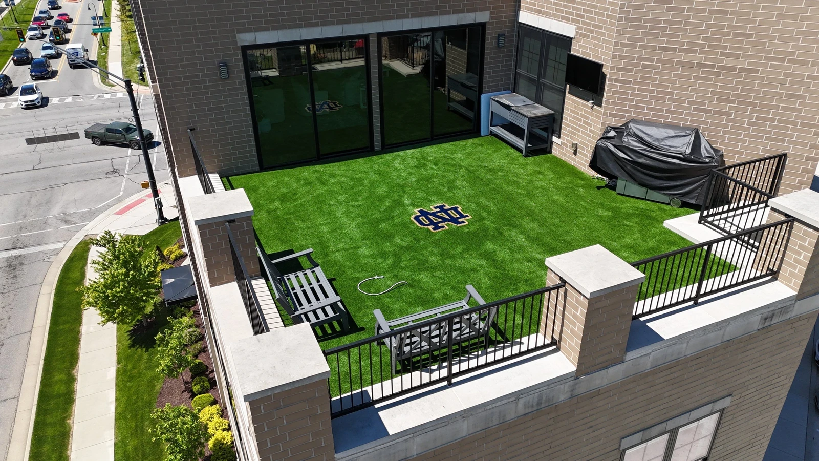 Rooftop terrace with 690 sq ft artificial SportsGrass turf featuring Notre Dame ND logo, grill, seating, and city street views below.