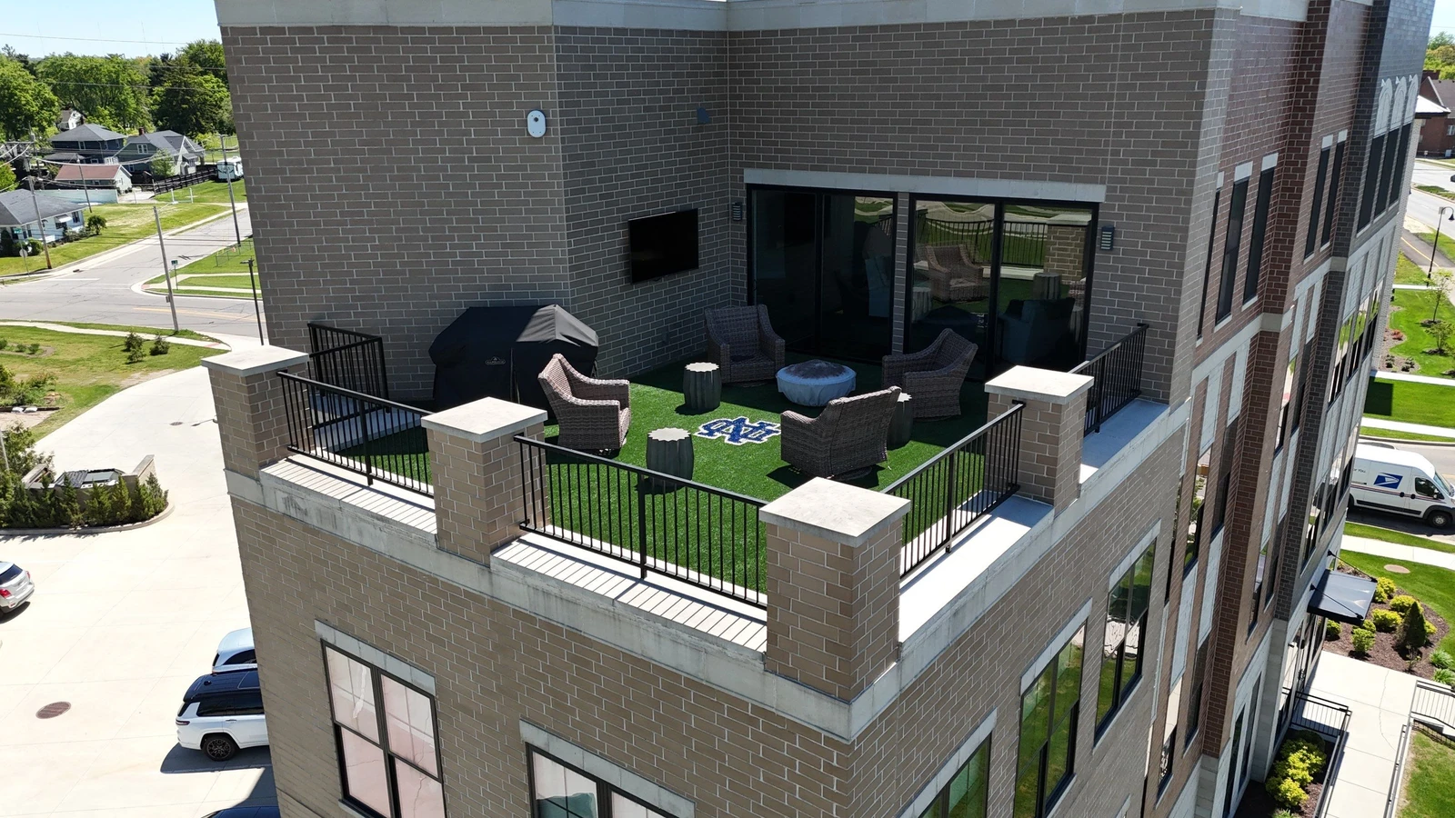 Rooftop terrace with 690 sq ft SportsGrass turf, wicker seating, fire pit, grill, and Notre Dame logo on modern brick building.